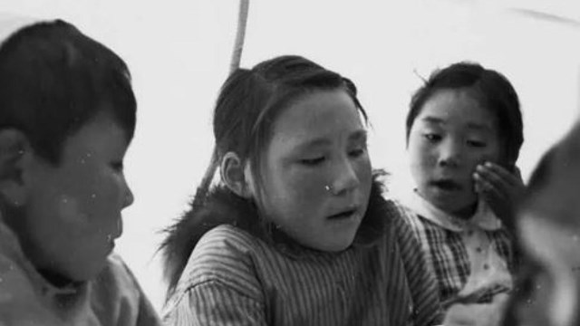 Three children -- a boy and two girls -- sit and look at an item held by the central child.