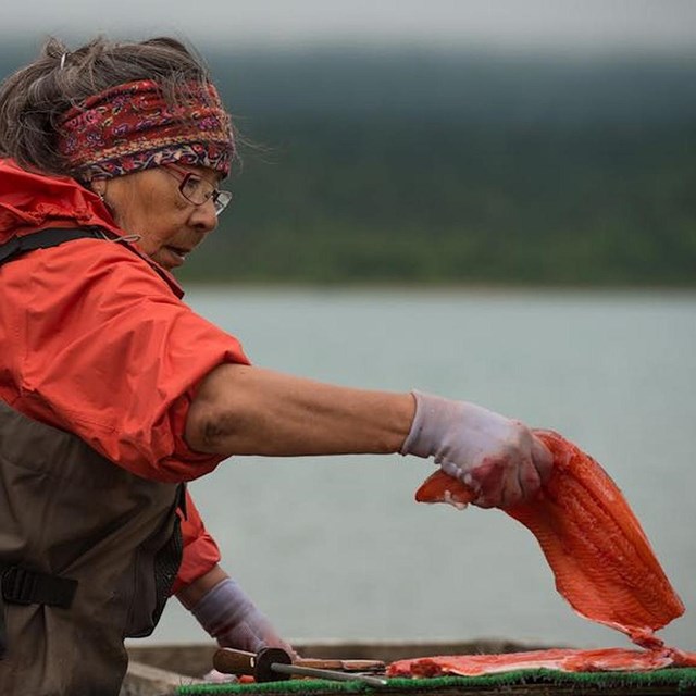 a young girl holds a piece of salmon by a river