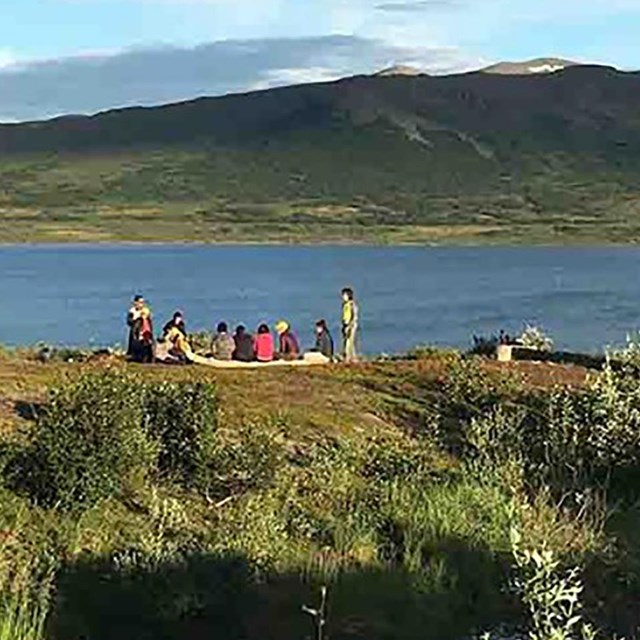 A group of people stand near a river, there is a metal structure nearby.