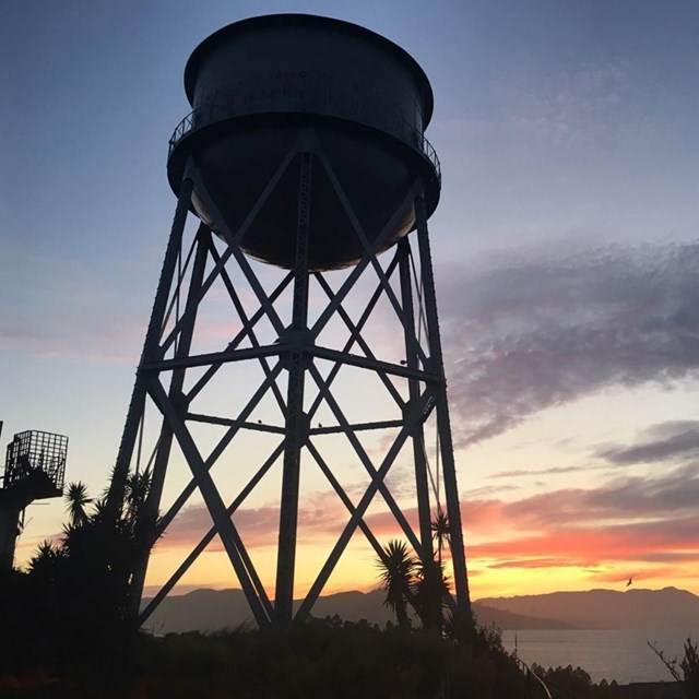 Silhouette of a water tower looms in the foreground with rosy sunset in background