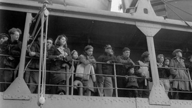 A historic scene of people lining the railing on a ship.