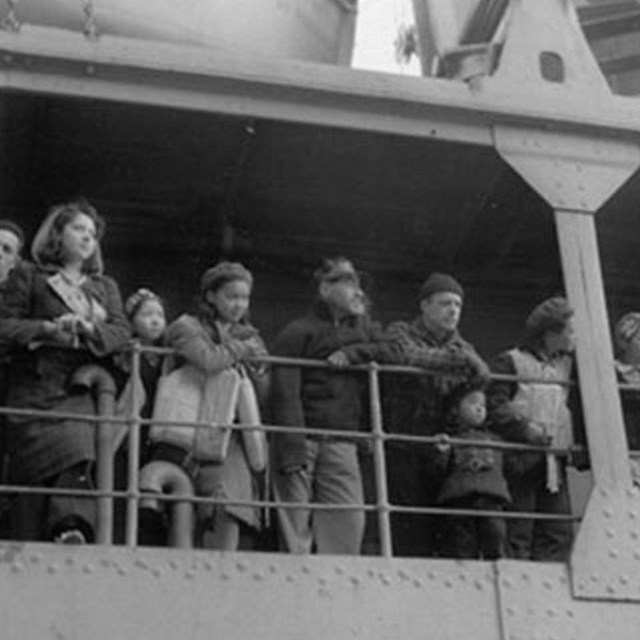 Black and white photo of people standing at boat railing.