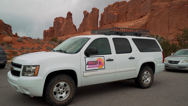 A white car with a visible logo sits at a trailhead in the park