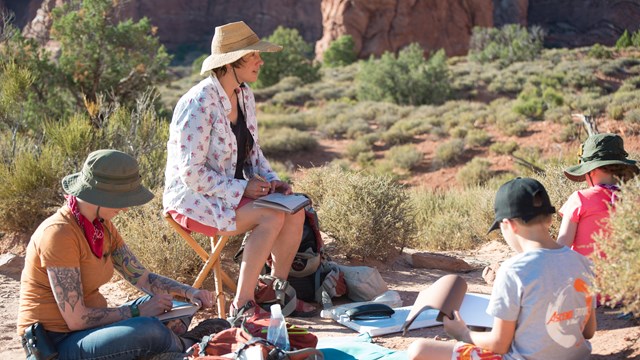 Three people sit outside while painting