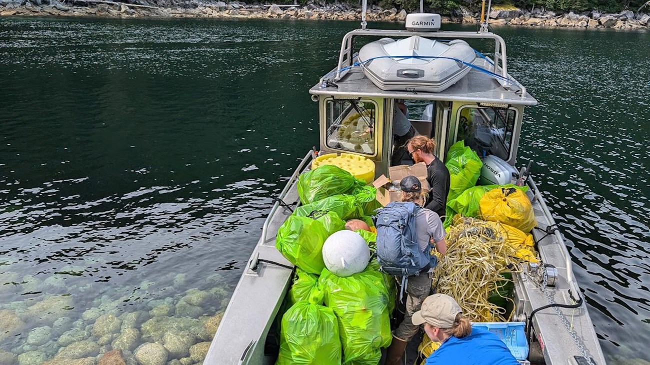 Three people fill a boat with bags of marine debris