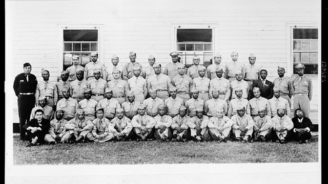 Grey Scale photo of men in uniform lined up infront of a wall standing in 4 rows