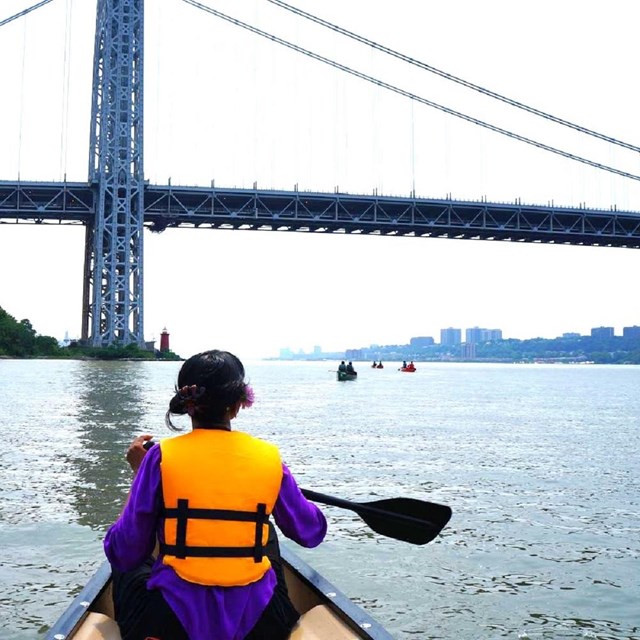 Kayaker approaching a bridge near a city skyline
