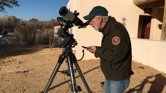 An NPS Volunteer looking into a telescope outside of the visitor center.