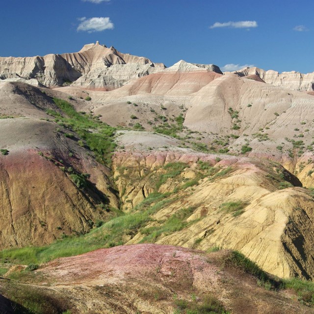 banded badlands buttes stretch far into the horizon with green prairie in valleys.