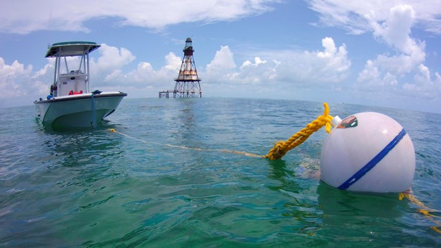 Boat attached to mooring buoy Fowey Rocks lighthouse in the distance