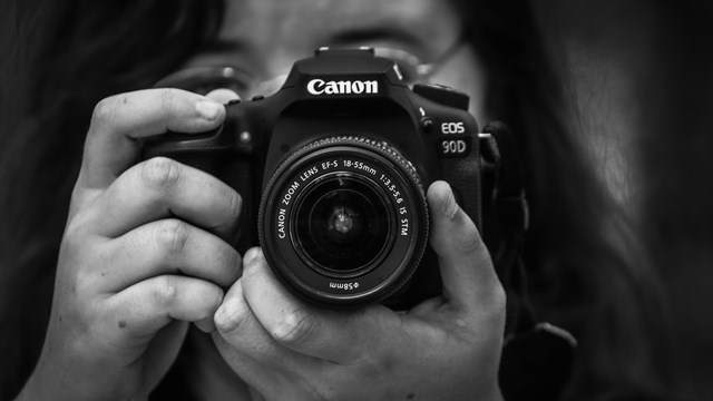 Black and white photo of a person holding their Canon digital camera with 2 hands.