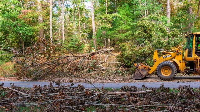 A large construction vehicle pushes storm debris off the road.