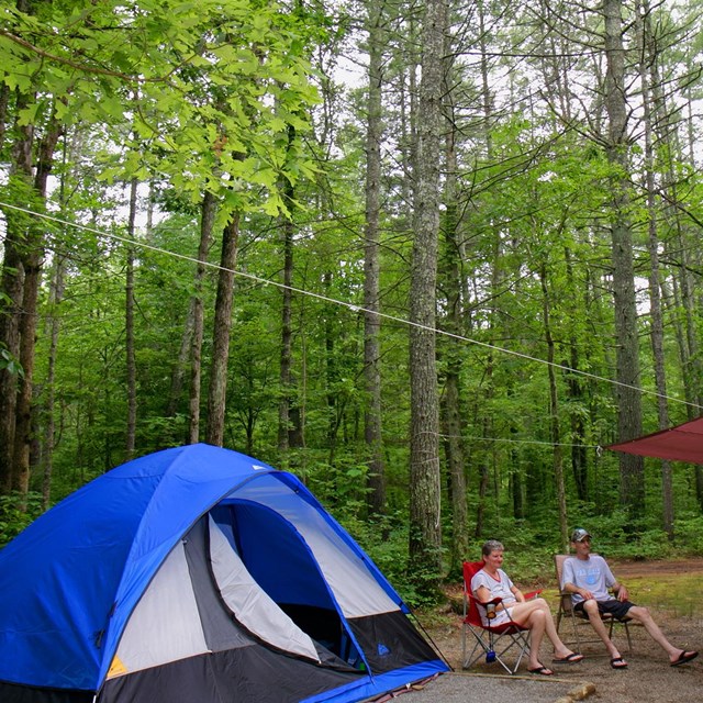 Two campers sitting in relaxing in folding chairs outside their tent.