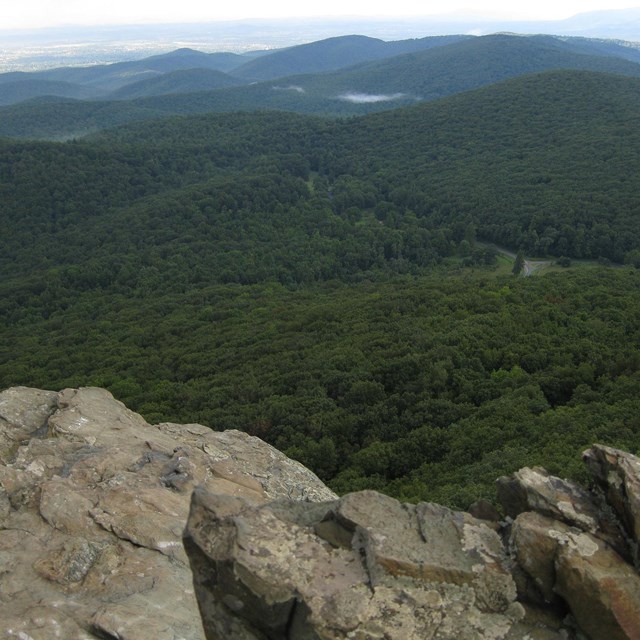 Bare rocks in the foreground with green, rolling mountains stretching off to the horiaon