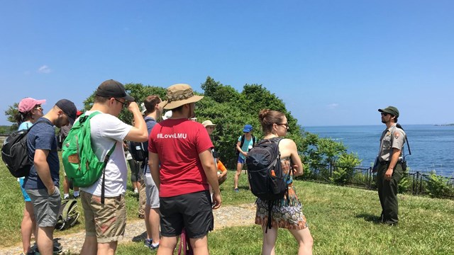 Ranger giving a talk to visitors with harbor in the background.