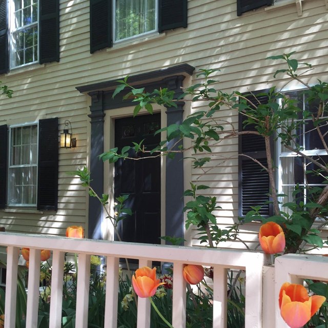 two story house with yellow siding and a white fence in front.