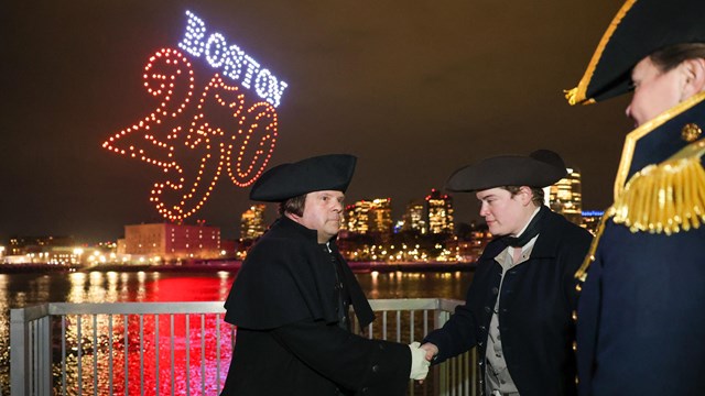A man as Paul Revere shakes hands with a reenactor and USS Constitution Commander.