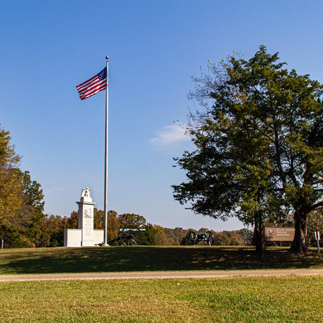 A grassy field, stone monument, and flying American flag.