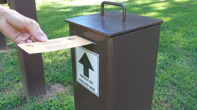 A hand drops a fee envelope into a fee box.