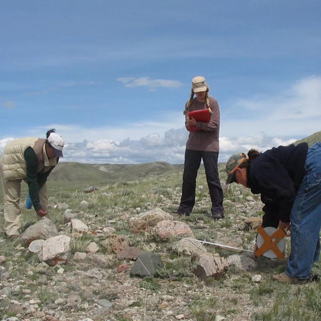 Three people standing around a cluster of rocks.