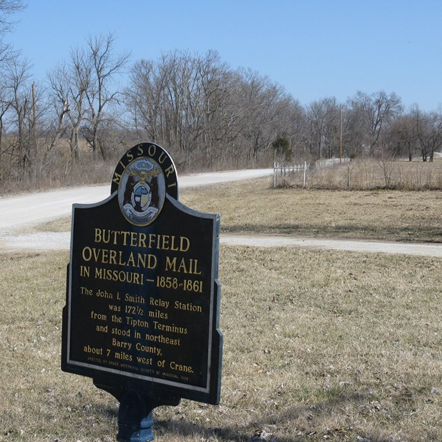 A large metal sign sitting in front of a field of grass.