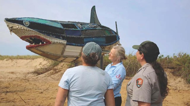 People look towards a shark sculpture.