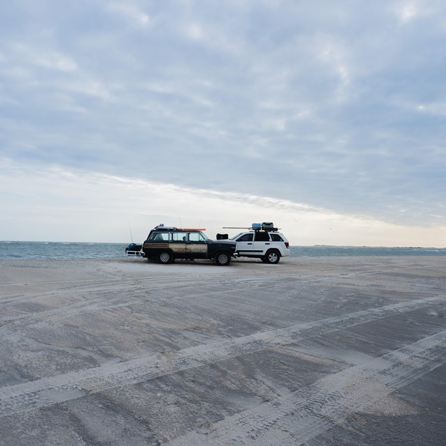 Two cars parks on sand during dusk. 