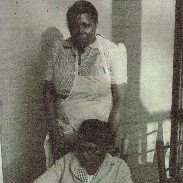 Woman stands, looking into camera. 