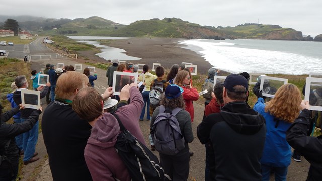 Crowd peers through transparent windows toward ocean beach on cloudy day