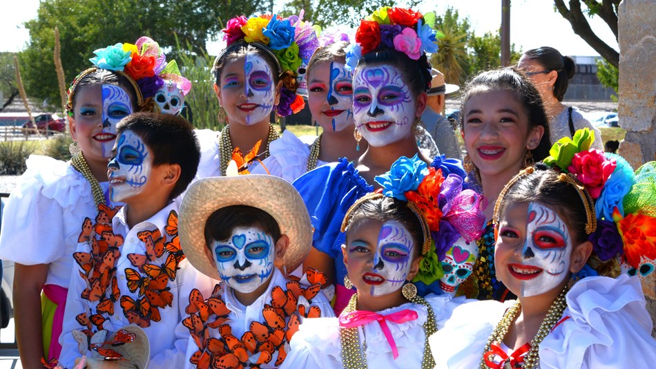 Folk dancers wearing traditional clothes, face paint, and floral headpieces.