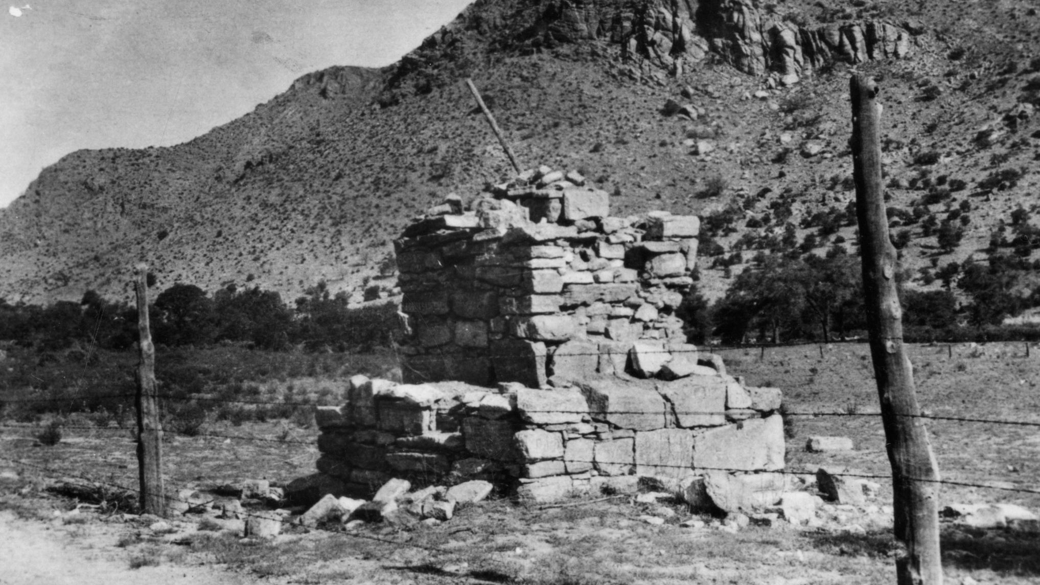 Three-tiered stone monument in a field behind a fence.