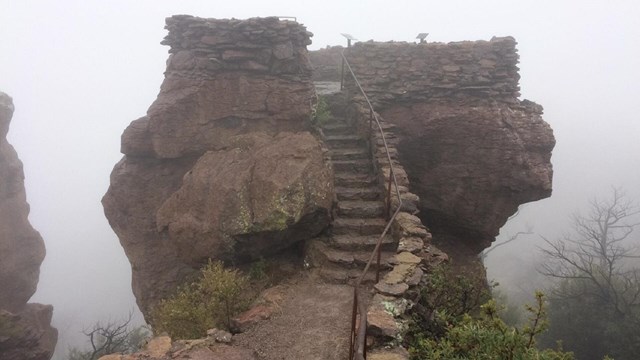 Stone steps leading to a platform on a large rock, in the fog. 