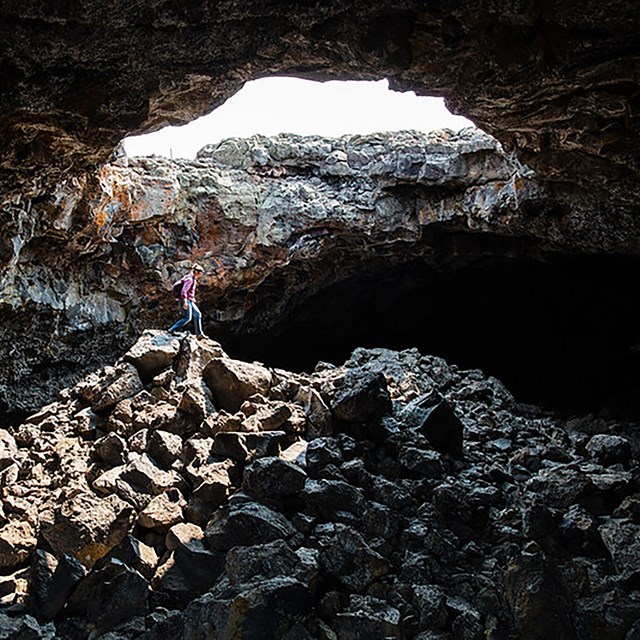 Caver walks over a pile of rocks underneath a sky light in a cave. 