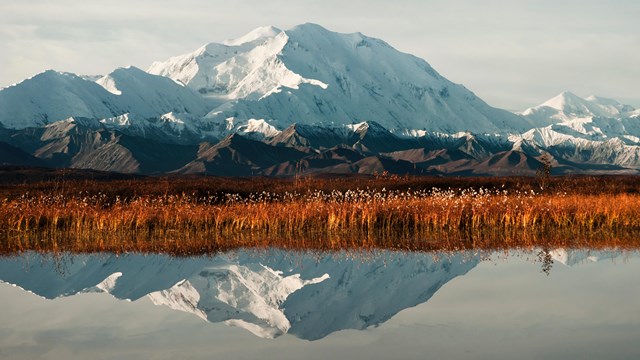 A mountain and reddish grasslands also reflected in a lake