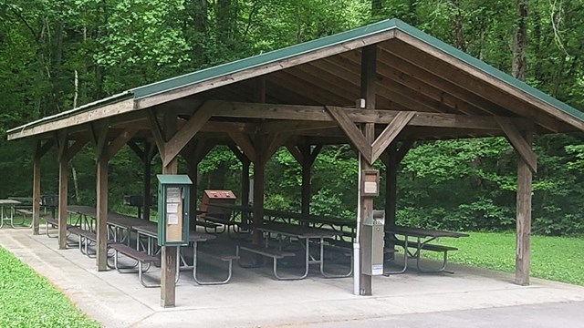 Picnic shelter in front of parking lot with green forest behind it. 