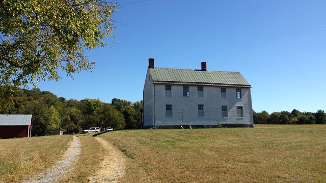 A dirt track leads towards a two-story farm house surrounded by low grass at Monocacy 