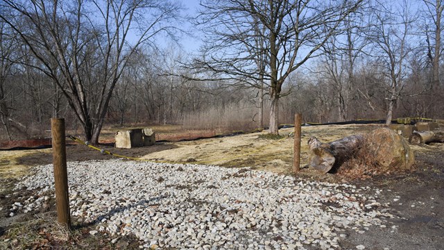 Cable gate blocks access across a white gravel driveway; the ground beyond covered in straw.