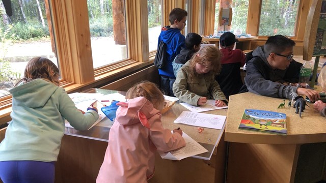 Kids work on coloring pages together around a table.