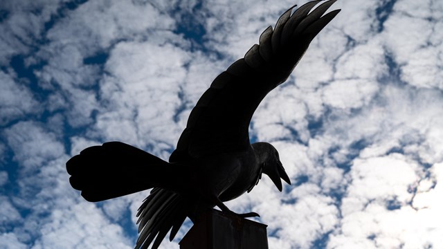 The raven statue appears ominously silhouetted against white fluffy clouds