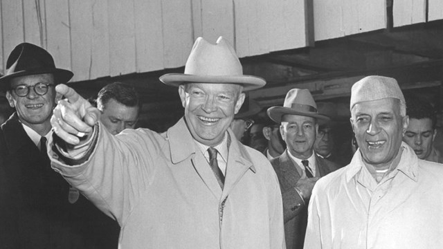 A black and white image of two men standing outside wearing overcoats, with one man pointing 