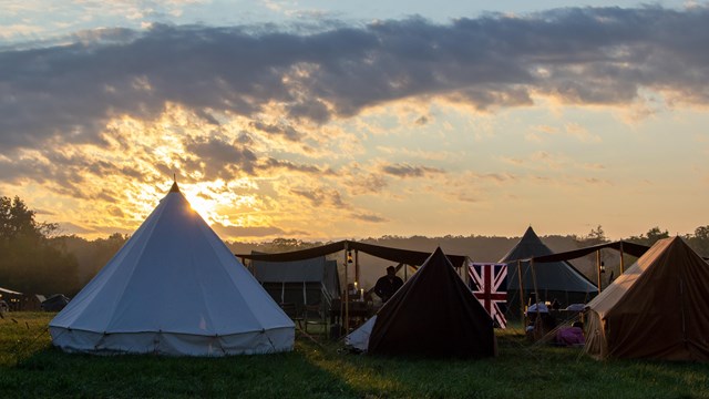 A color image showing army tents with a yellow sunrise in the background