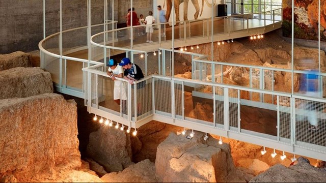 Two boys peering off a hanging boardwalk over an excavation site