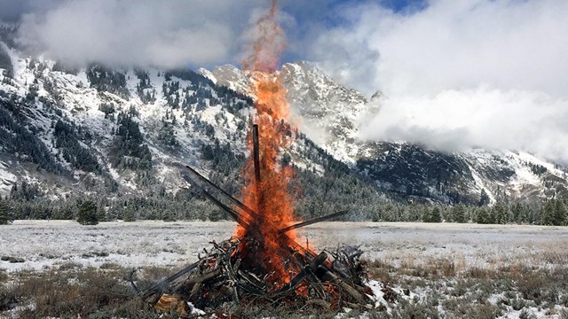 slash fire on a sunny day with snowy mountains