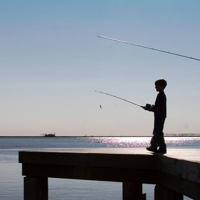 child and father fishing off of dock into ocean. 