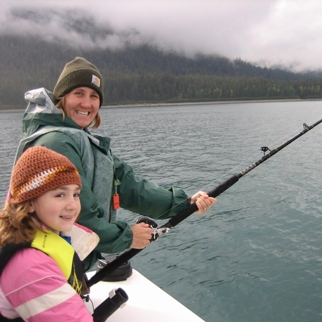 Woman and girl fish from boat in a bay.