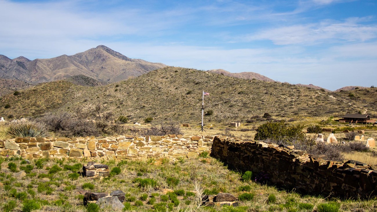 Rock and adobe ruins, a one-story visitor center sits on the far right, mountains in background