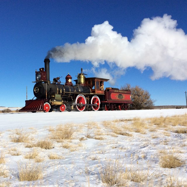 A black and red train with smoke coming out of the stack.