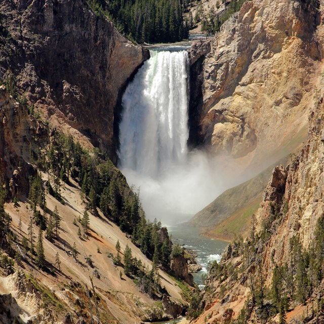 A waterfall crashes down into a tan canyon.