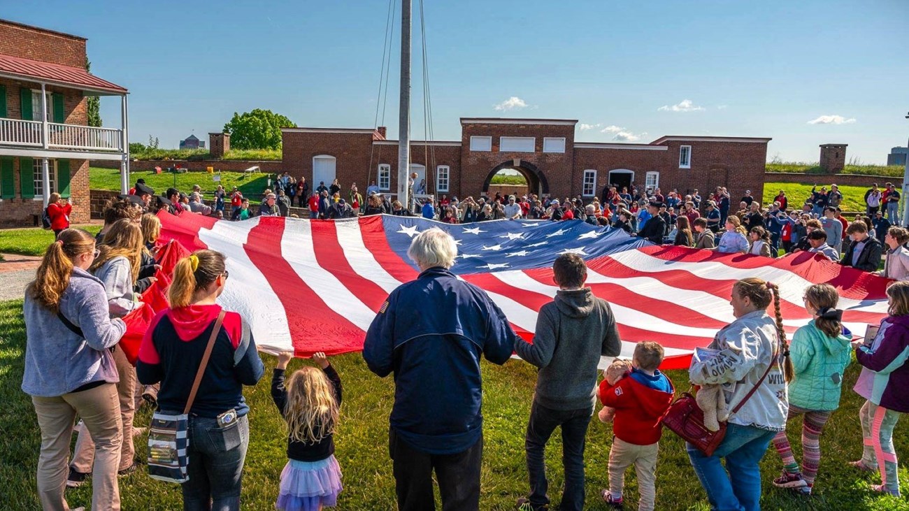 Large group of visitors assisting with folding a large American flag