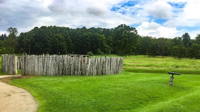 A wooden stockade and earthworks in a meadow.